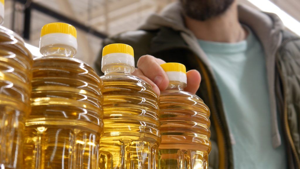 closeup beautiful sunflower oil bottles store male buyer takes one - سمن نباتي شورتنج المكون السري لطهي مثالي